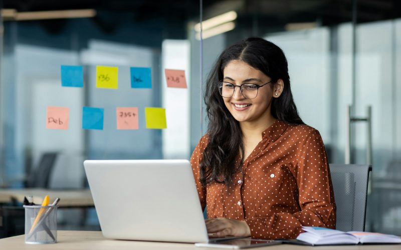 Happy and smiling hispanic businesswoman typing on laptop, office worker with curly hair and